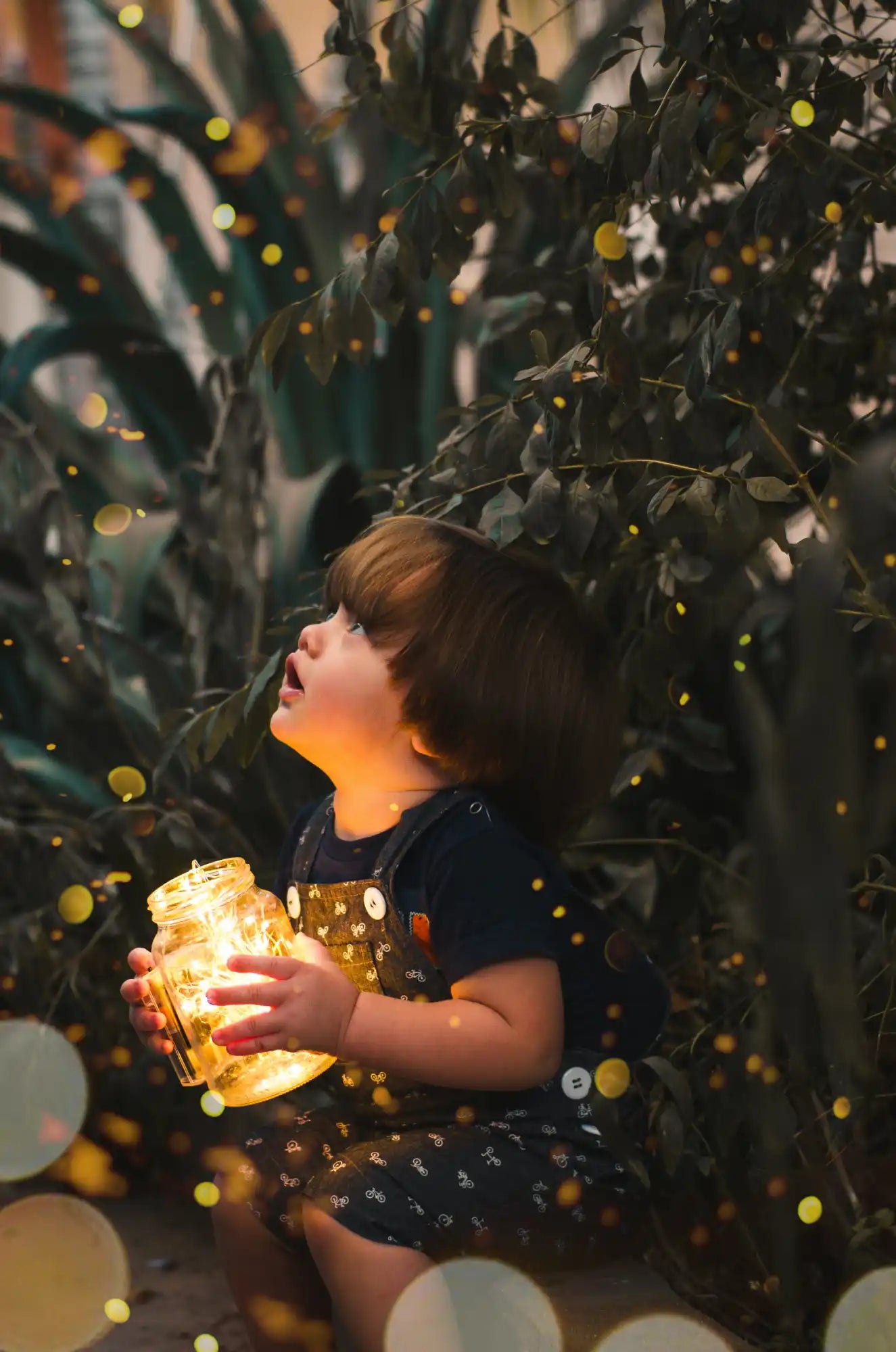 Un enfant tenant un pot lumineux de lumières tout en regardant vers le haut.