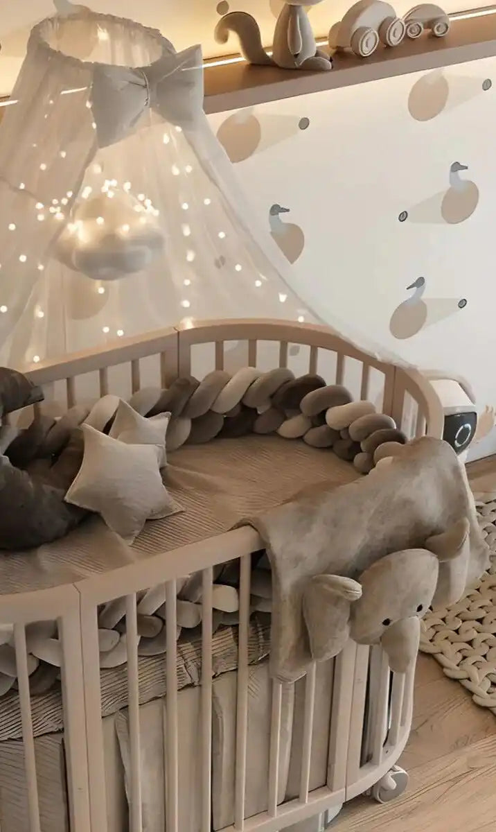 Berceau en bois blanc rond avec un auvent en tulle et des guirlandes lumineuses.